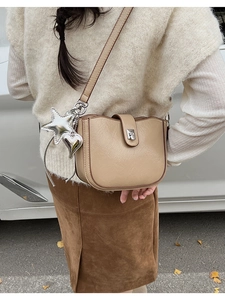 Detailed view of apricot saddle bag with silver star and heart charms on a leather strap
