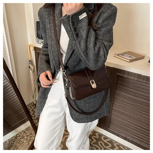 Close-up of deep brown glossy leather bag with gold buckle on grey wool blazer