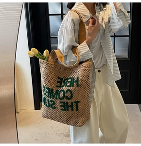 Detail of woven straw tote bag featuring green Here Comes The Sun embroidery and brown strap