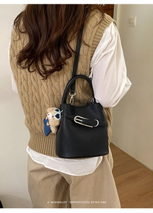Detail of black lychee leather bucket bag with metal buckle and cute bear charm