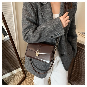 Detail of dark brown leather crossbody bag with a metallic gold oval clasp on grey blazer