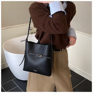 Gros plan du sac seau noir en cuir grainé avec boucle dorée et détails du logo blanc