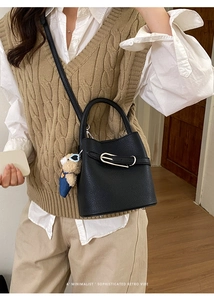 Detail of black lychee grain bucket bag with silver buckle and cute bear charm decoration