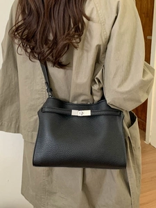 Sac seau chic en cuir grainé noir avec fermoir argenté porté sur l'épaule d'un modèle