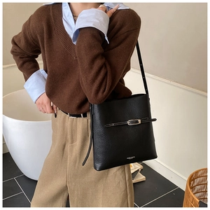 Détail du sac seau noir en cuir grainé avec boucle décorative et logo doré chic