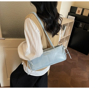 Close-up of light blue baguette bag with dual thin straps and metal brand plate detail