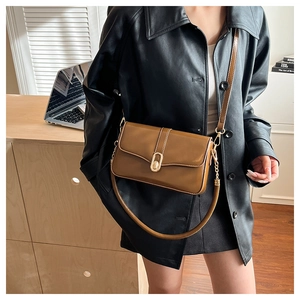 Detail of a brown leather crossbody bag featuring a golden oval twist lock and dual straps
