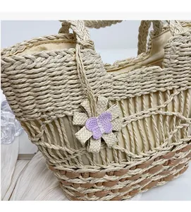 Dettaglio della borsa in paglia intrecciata con finiture marroni e fiore a farfalla viola