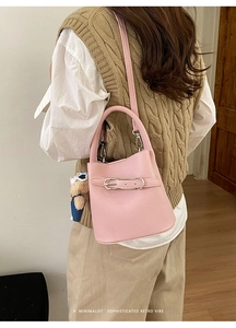 Pink bucket bag with belt buckle detail and bear charm shown on a casual model outfit