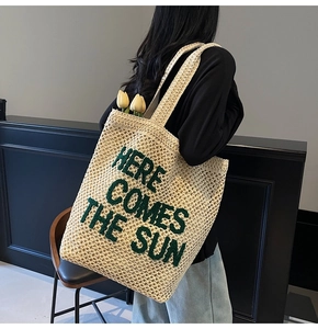 Detail of woven straw tote bag with Here Comes The Sun green text and tulip decoration