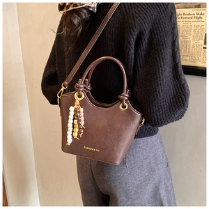 Detailed view of deep brown bucket bag with fashion logo and beaded tassel charm