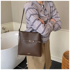 Détail d'un sac seau marron foncé en cuir grainé avec une boucle en métal doré chic