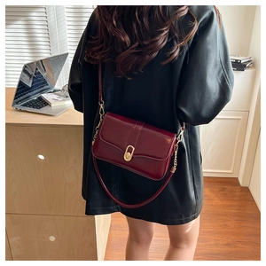 Detail view of burgundy leather bag with gold buckle worn on shoulder in office setting
