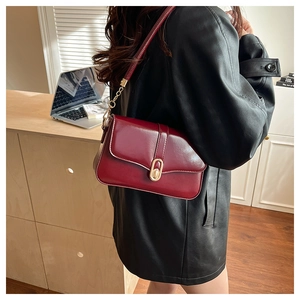 Detail of burgundy glossy leather handbag with gold oval buckle and chain strap