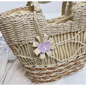 Détail d'un sac de plage en paille avec fleur tressée et papillon en crochet violet élégant