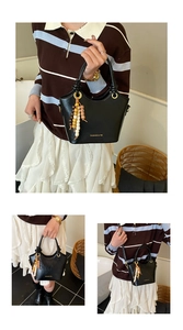 Detalle de bolso bucket de cuero negro con asas de anillo dorado y borla de cuentas