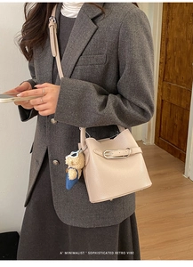 Detail view of beige lychee leather bucket bag with cute bear charm and metal buckle