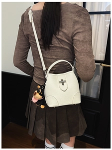 Close-up of a white lychee leather bucket bag with a metal twist lock and puppy charm