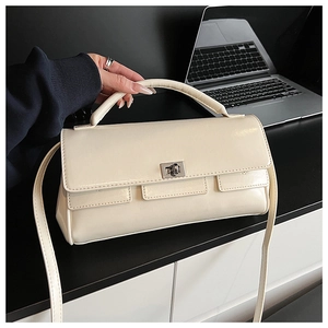 Detail of cream flap handbag with metallic rotary lock and three decorative front pockets