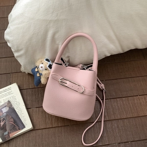 Detail of pink lychee leather bucket bag with teddy bear charm on wood floor