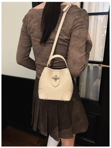 Detail of cream beige lychee leather bucket bag with silver buckle worn as a crossbody