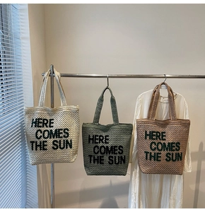 Detail view of woven beach tote bags in various colors with Here Comes The Sun embroidery