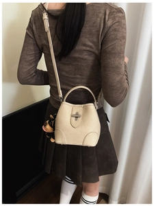Detail view of cream bucket bag with litchi grain leather and metal twist lock closure