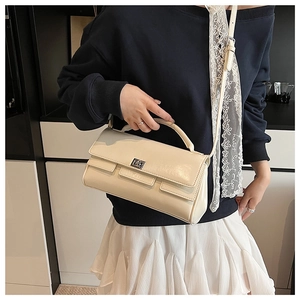 Detail of a beige flap handbag with silver turn-lock clasp shown on a model's shoulder
