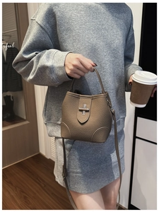 Detail view of brown pebbled leather bucket bag with metallic twist lock in casual setting