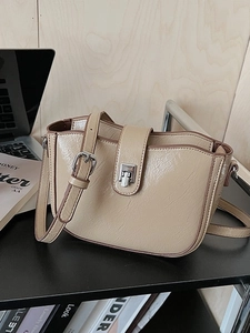 Minimalist beige bucket bag with silver buckle and adjustable strap on a wooden desk