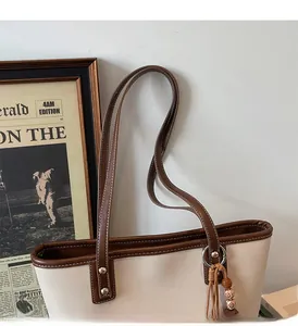 Close-up of cream tote bag with brown handles and a wooden bead tassel charm