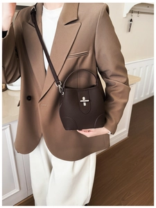 Detail of dark brown lychee leather bucket bag featuring a silver cross-shaped metal lock