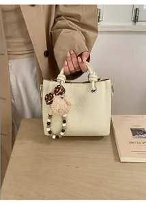 Dettaglio borsa beige a grana litchi con ciondolo di peluche e manico di perline