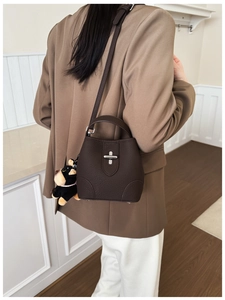 Detail of dark brown pebble leather bucket bag with silver cross lock and plush dog charm