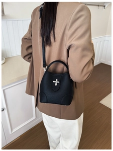 Detailed view of black litchi pattern bucket bag with silver cross buckle worn on shoulder