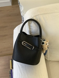 Black lychee leather bucket bag with silver buckle and bear charm on white sofa