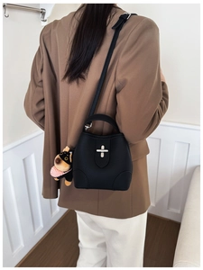 Close-up of black litchi leather bucket bag with silver cross lock and plush dog charm