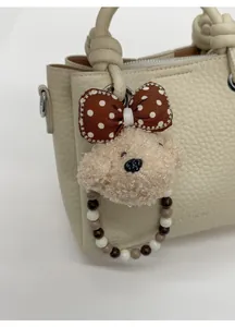 Dettaglio di un simpatico ciondolo a forma di cane di peluche con perline su borsa crema