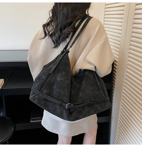Detail of a large black suede tote bag with horizontal leather strap and buckle hardware