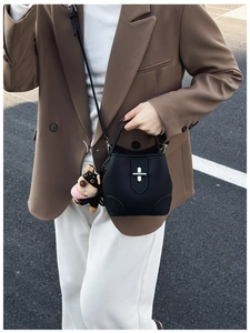 Detail view of a black lychee leather bucket bag with silver lock and plush puppy charm
