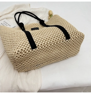 Top view of hollow woven straw tote bag with black strap handles on white cloth