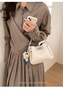 Close-up of beige lychee leather bucket bag featuring a metal lock and cute bear charm