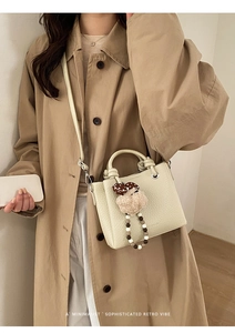 Dettaglio borsa a secchiello in pelle crema con ciondolo a perle su trench kaki