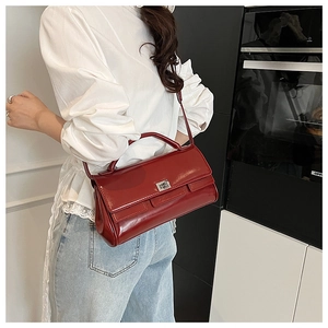Detail of burgundy glossy leather handbag with square metal buckle and flap design