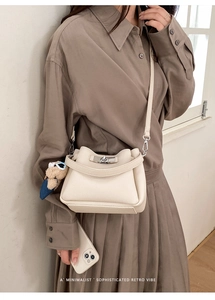 Detail of cream lychee leather bucket bag with silver twist lock and blue bear charm