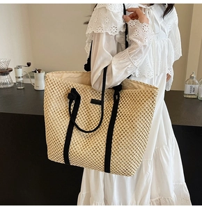 Detail of hollow woven tote bag featuring thick black cotton rope handles and beige straw texture