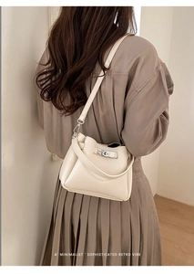 Detail of cream lychee leather bucket bag with silver rotating lock on brown dress