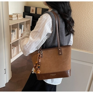 Detail of retro suede and leather tote bag with wooden bead charm in a cozy library setting