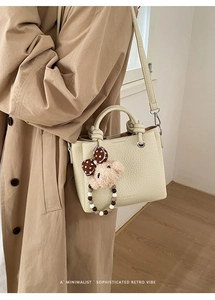 Dettaglio della borsa tote beige con texture litchi e un simpatico ciondolo a forma di orsetto