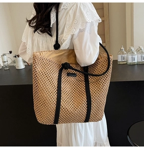 Detailed shoulder view of a large woven straw tote bag with black rope straps for beach
